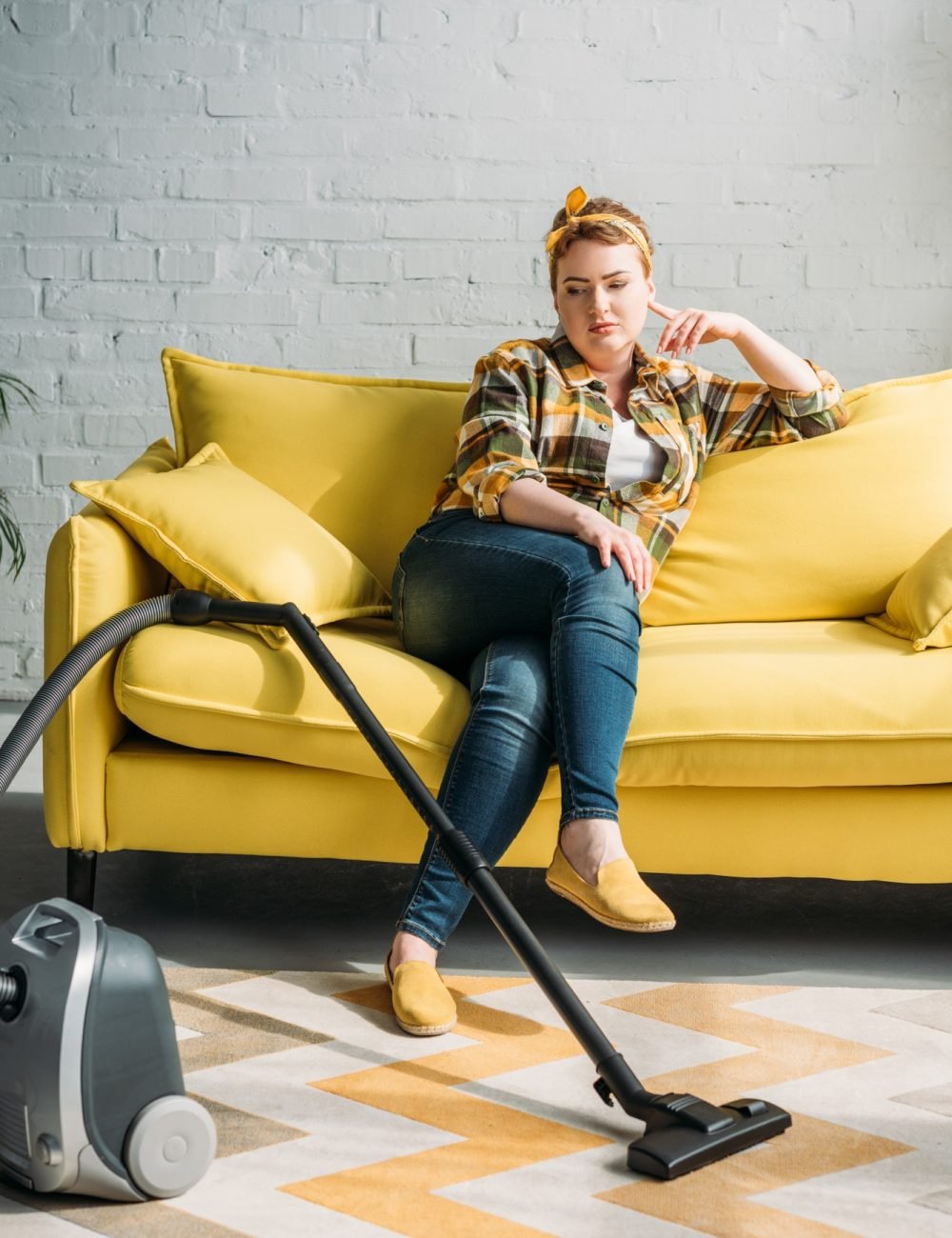 beautiful woman sitting on sofa and looking at vacuum cleaner at home