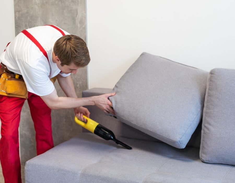Handsome young man cleaning furniture. Process of deep furniture cleaning, removing dirt from sofa